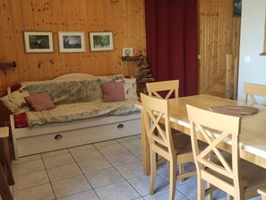 A wooden interior with a sofa, dining table, chairs, and framed pictures on the wall.