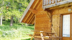 A wooden cabin with a balcony, a wooden deck, and a door with glass panels.
