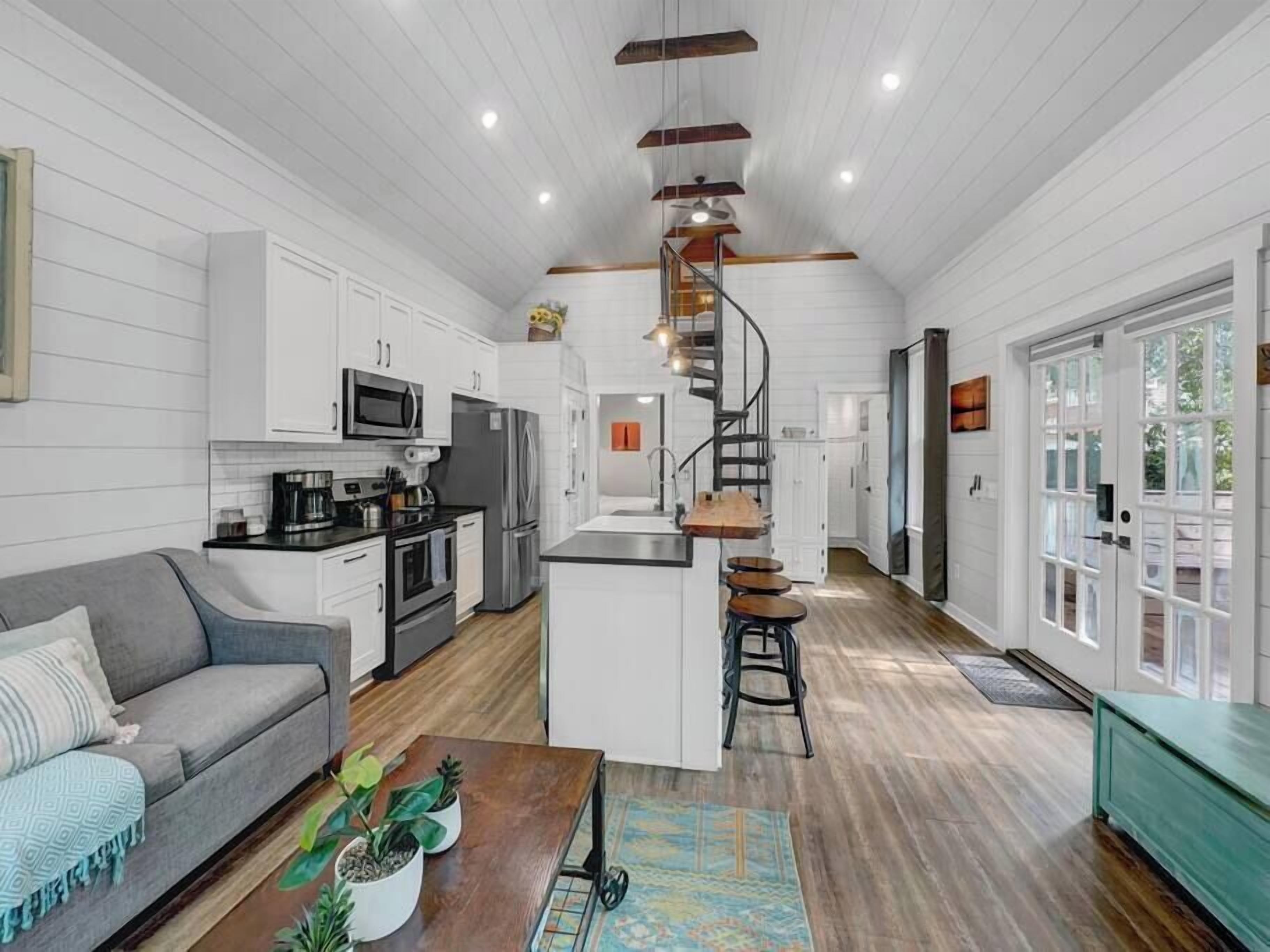 Una cocina moderna con armarios blancos, una isla central y una escalera en espiral.