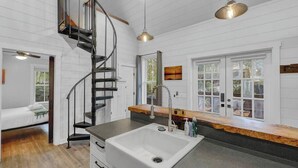 A modern kitchen with a central island, a spiral staircase, and a large window providing natural light. - Private Hot Tub Island Cottage Near Folly Beach (Charleston)