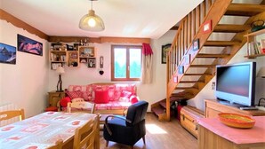 A cozy living room with a wooden staircase, a dining table, and a television. - Family chalet in La Joue du Loup with parking (La Joue du Loup)