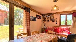 A cozy room with a dining table, chairs, a sofa, and a window with a view of the outdoors. - Family chalet in La Joue du Loup with parking (La Joue du Loup)