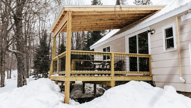 A wooden deck with a railing, a covered area, and a house in the background. - Rental gateway in UP (Nisula)