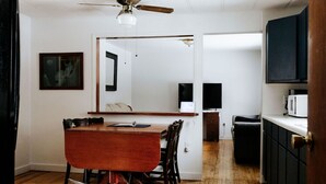 A dining area with a wooden table and chairs, a ceiling fan, and a kitchen area with cabinets and a microwave. - Rental gateway in UP (Nisula)