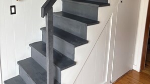 A staircase with dark steps and a wooden handrail, leading to a white door with a small black square feature. - Rental gateway in UP (Nisula)