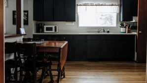 A kitchen with dark cabinets, a wooden dining table, chairs, a microwave, and a window with a curtain. - Rental gateway in UP (Nisula)