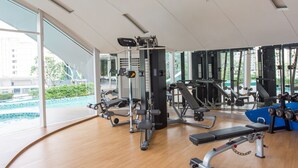 Un gimnasio moderno con diversas máquinas de ejercicio, ventanas amplias y suelo de madera.