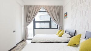 Una habitación de hotel con un ventanal grande, dos camas con ropa de cama blanca y almohadas amarillas, un cabecero gris y un papel tapiz estampado.