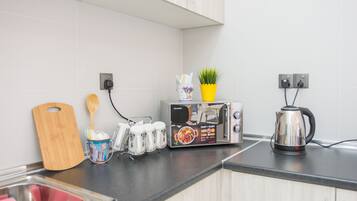 A kitchen with a toaster, a kettle, a wooden cutting board, a plant, and a cup holder with utensils.