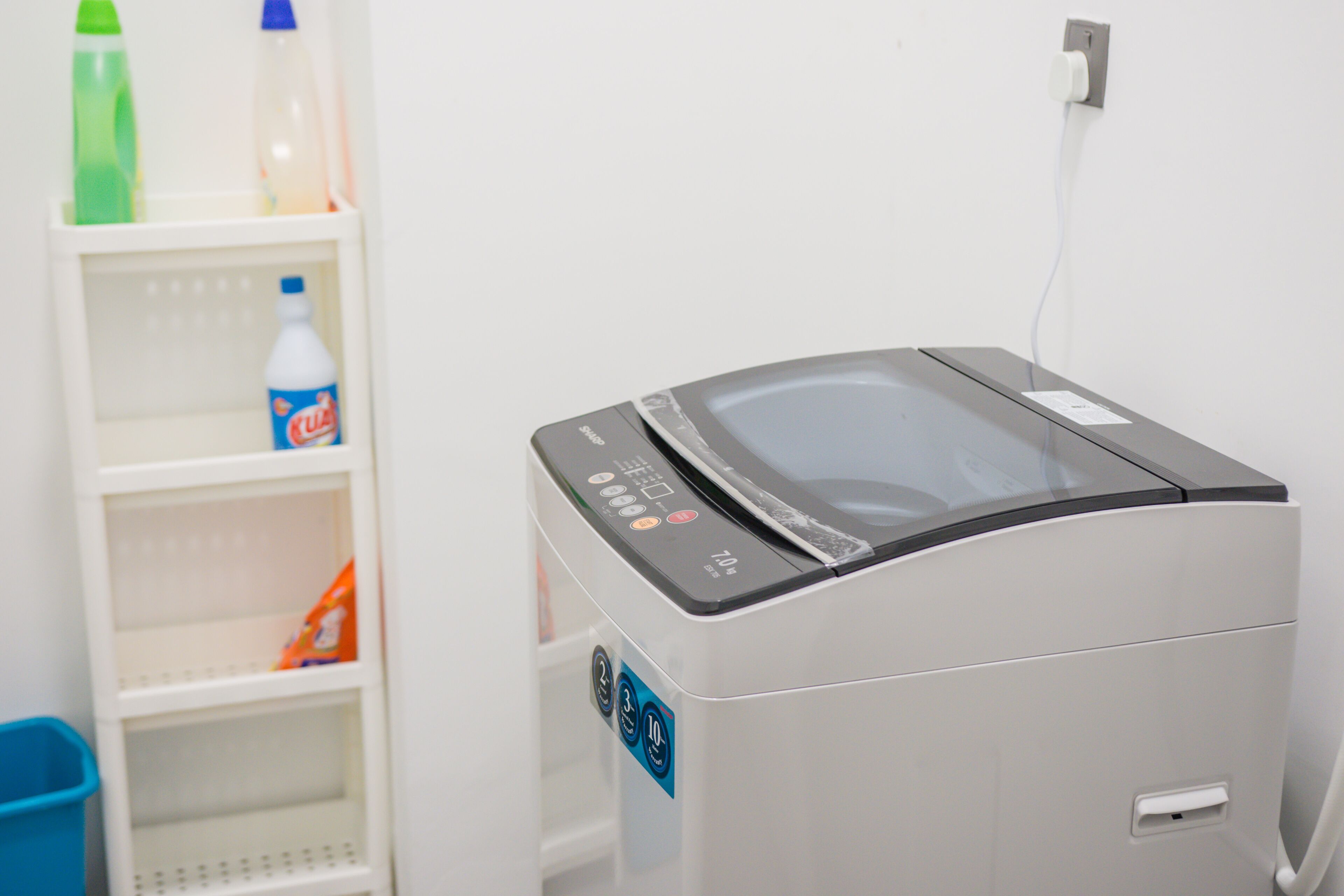 Un lave-linge compact et moderne, doté d’un panneau de commande, placé à côté d’une étagère blanche sur laquelle se trouvent divers objets.