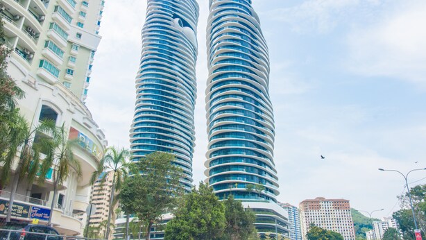 Dos rascacielos altos y cilíndricos con un diseño moderno, rodeados de palmeras y otros edificios.
