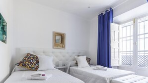 Een hotelkamer met twee bedden, een wit hoofdbord, een klein tafeltje en een raam met blauwe gordijnen.