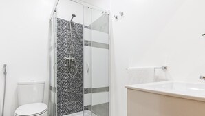 Een moderne badkamer met een douchecabine van glas, een wit toilet en een beige wastafel.