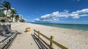 A beach with a wooden fence, a planter, and a hotel in the background. - Oceanfront, heated pool & Sea Breeze balcony (Hollywood)