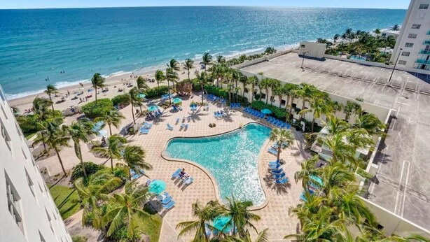 A pool area with lounge chairs and palm trees, overlooking a beach and ocean. - Oceanfront, heated pool & Sea Breeze balcony (Hollywood)