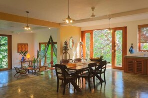 A spacious dining area with a large table and chairs, a chandelier, and a view of greenery through the windows. - Highland Villa (Weligama)