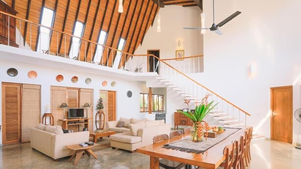 A spacious living area with a high ceiling, a wooden staircase, and a dining table set for six. - Highland Villa (Weligama)