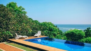 A swimming pool with two white lounge chairs, surrounded by greenery and overlooking the ocean. - Highland Villa (Weligama)
