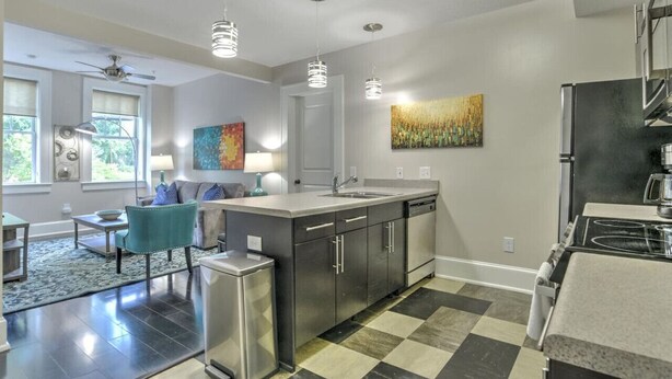 A modern kitchen with stainless steel appliances, a central island, pendant lighting, and a checkered floor. - Charming Historic King James Building Unit #4 (Asheville)