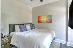 Una camera da letto con un letto, un comodino, una sveglia a parete e un quadro astratto dai colori vivaci.
