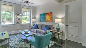 A living room with a gray sofa, teal armchair, and a colorful abstract painting on the wall. - Charming Historic King James Building Unit #4 (Asheville)