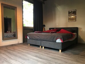 Relax in a serene bedroom with a large bed, wooden floor, and a large mirror.