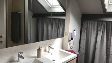 Une salle de bain avec un grand miroir, deux lavabos, un porte-serviettes, un rideau de douche et un luminaire au plafond.