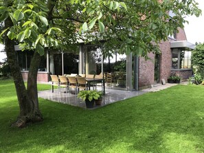 A covered outdoor dining area with a glass enclosure, a brick building, and a well-maintained lawn. - Grysperre B&B (Hooglede)
