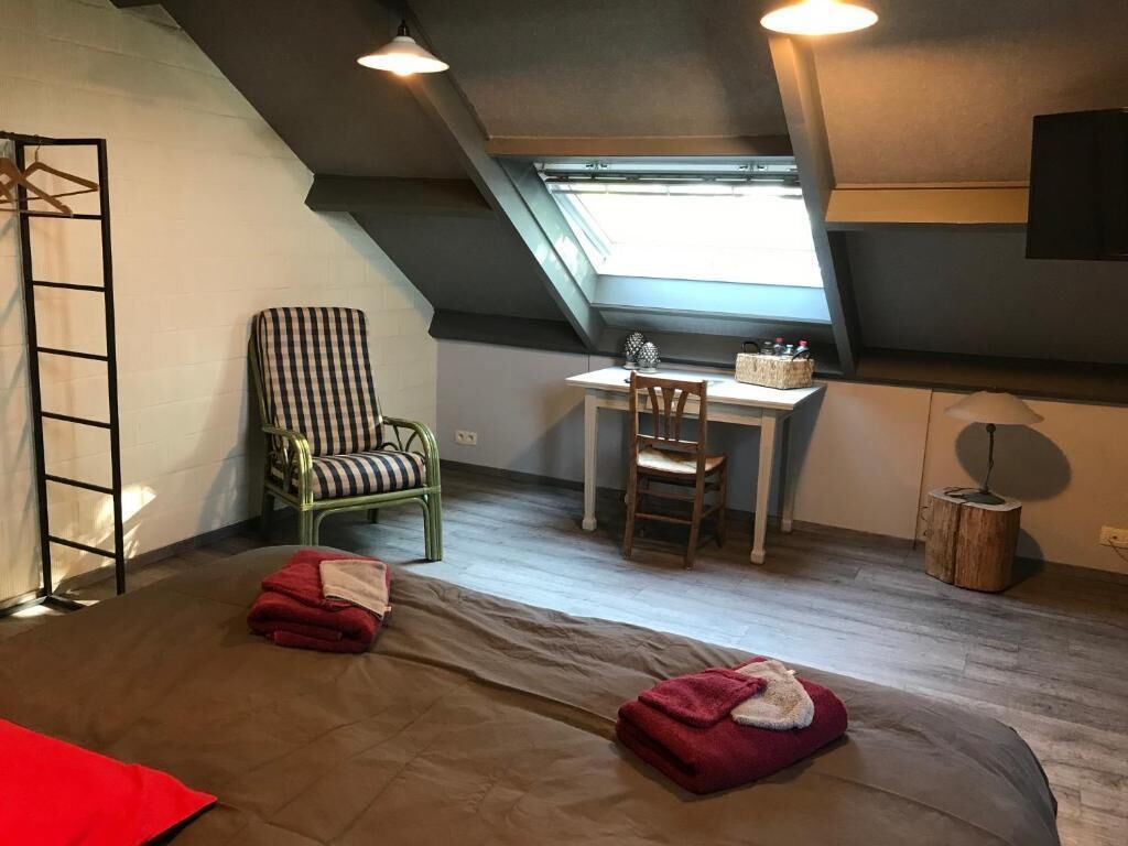 Una habitación estilo loft con techo inclinado, un escritorio con silla, una ventana y una escalera.