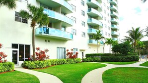 A multi-story hotel with a curved facade, balconies, and a well-maintained lawn with pathways. - SUNNY ISLES CONDO-RESORT (PARKING INCLUDED) (Sunny Isles Beach)