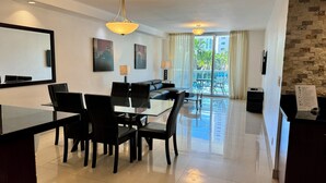 A modern hotel room with a dining area, a sofa, and a balcony with a view of palm trees. - SUNNY ISLES CONDO-RESORT (PARKING INCLUDED) (Sunny Isles Beach)