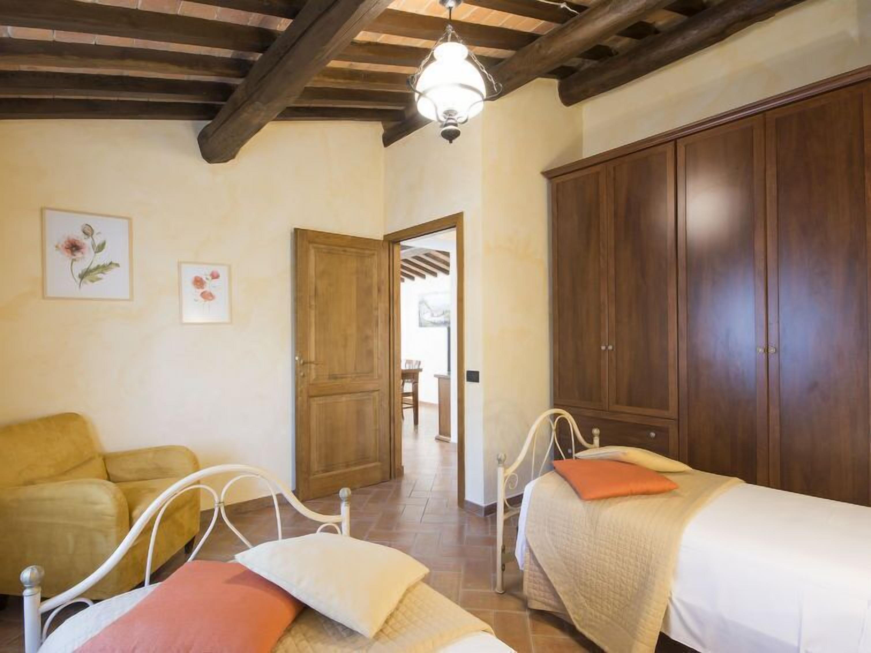 A bedroom with two beds, a wooden wardrobe, a yellow armchair, and a ceiling fan.