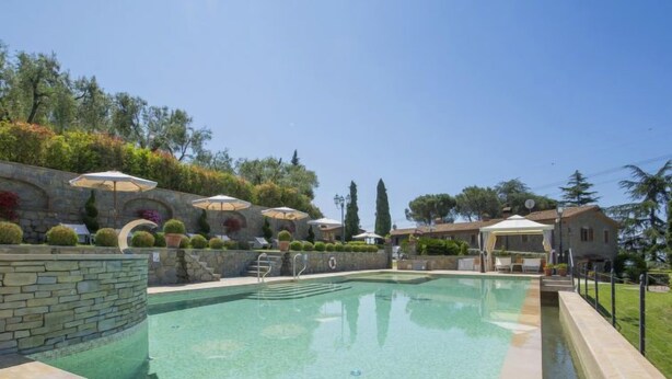Ein Pool mit Steinwänden und -terrasse, umgeben von Sonnenschirmen und Topfpflanzen.