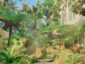 A lush garden with a variety of ferns and flowering plants, a small stream, and a stone wall. - ANA Park (Chiang Mai)