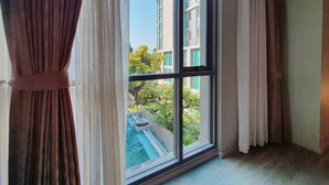 Una habitación con un ventanal grande, cortinas y vistas a un edificio y vegetación.