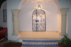 A white door with intricate metalwork, flanked by two columns and a small light above.