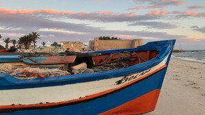 A beach with a row of boats, a sandy shore, and a distant fortification. - La maison des oliviers (Hammamet)