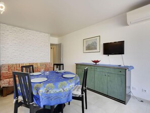 Un coin repas avec une table ronde dressée pour quatre personnes, un meuble vert, un téléviseur à écran plat fixé au mur et un canapé à motifs en arrière-plan.