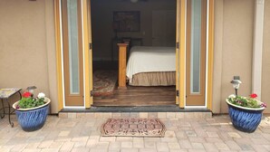 A hotel entrance with a sliding glass door leading to a bedroom. There are two large flower pots on either side of the door, a welcome mat in front, and a ceiling fan in the room. - Robin`s Red Rock Getaway Suite A (Sedona)