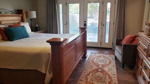 A bedroom with a wooden bed, a nightstand with a lamp, a dresser, and a view through a glass door to the outside. - Robin`s Red Rock Getaway Suite A (Sedona)
