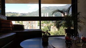 Una sala de estar con un sofá, una mesa de centro redonda y vistas de un paisaje urbano a través de amplios ventanales.