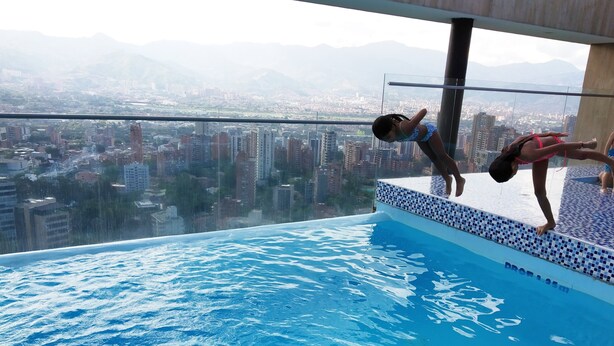 Una piscina infinita en la azotea con vistas a la ciudad, barandilla de cristal y borde de azulejos.