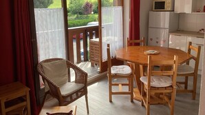 A cozy kitchen with a wooden table and chairs, a red curtain, and a view of a green landscape through a sliding glass door. - Abondance: 4-person apartment in the heart of the Abondance valley (Abondance)