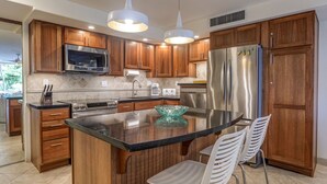 A modern kitchen with wooden cabinets, stainless steel appliances, a central island with chairs, and pendant lighting. - Dine in paradise on your garden-view lanai (Lahaina)