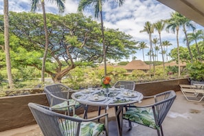A covered outdoor dining area with a round table and chairs, surrounded by lush greenery and palm trees.