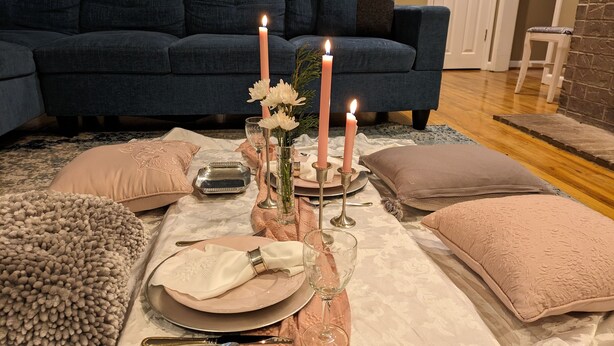 Une table dressée pour un repas, avec une nappe rose et beige, un vase rempli de fleurs et trois bougies allumées.