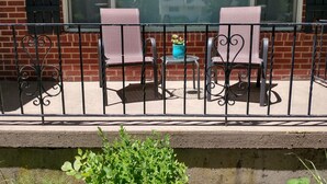 Un balcon avec deux chaises et une petite table, une plante en pot et un mur de briques avec des fenêtres.