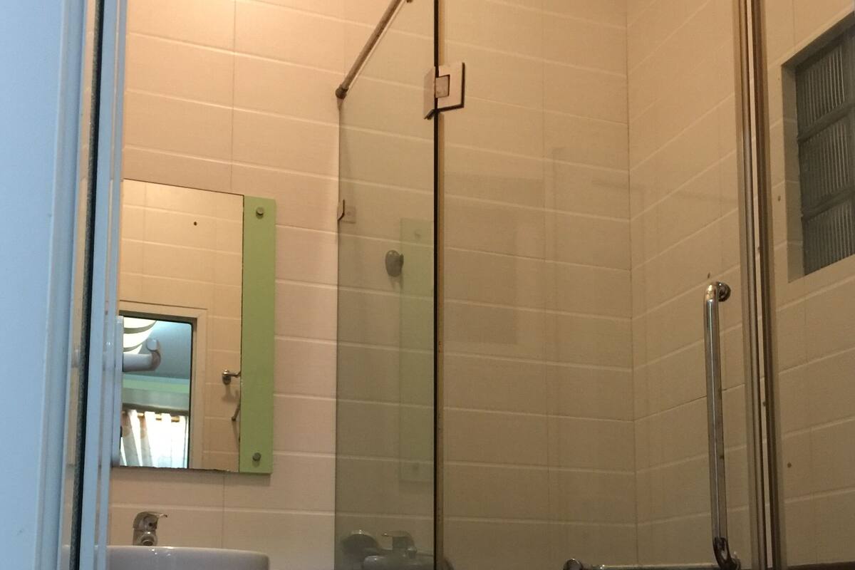 A bathroom with a glass shower enclosure, a sink with a mirror, and dark tiled walls.