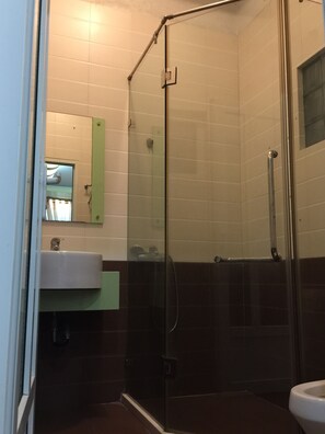 A bathroom with a glass shower enclosure, a sink with a mirror, and dark tiled walls. - AB Lake Side Ho An Bien (Hai Phong)
