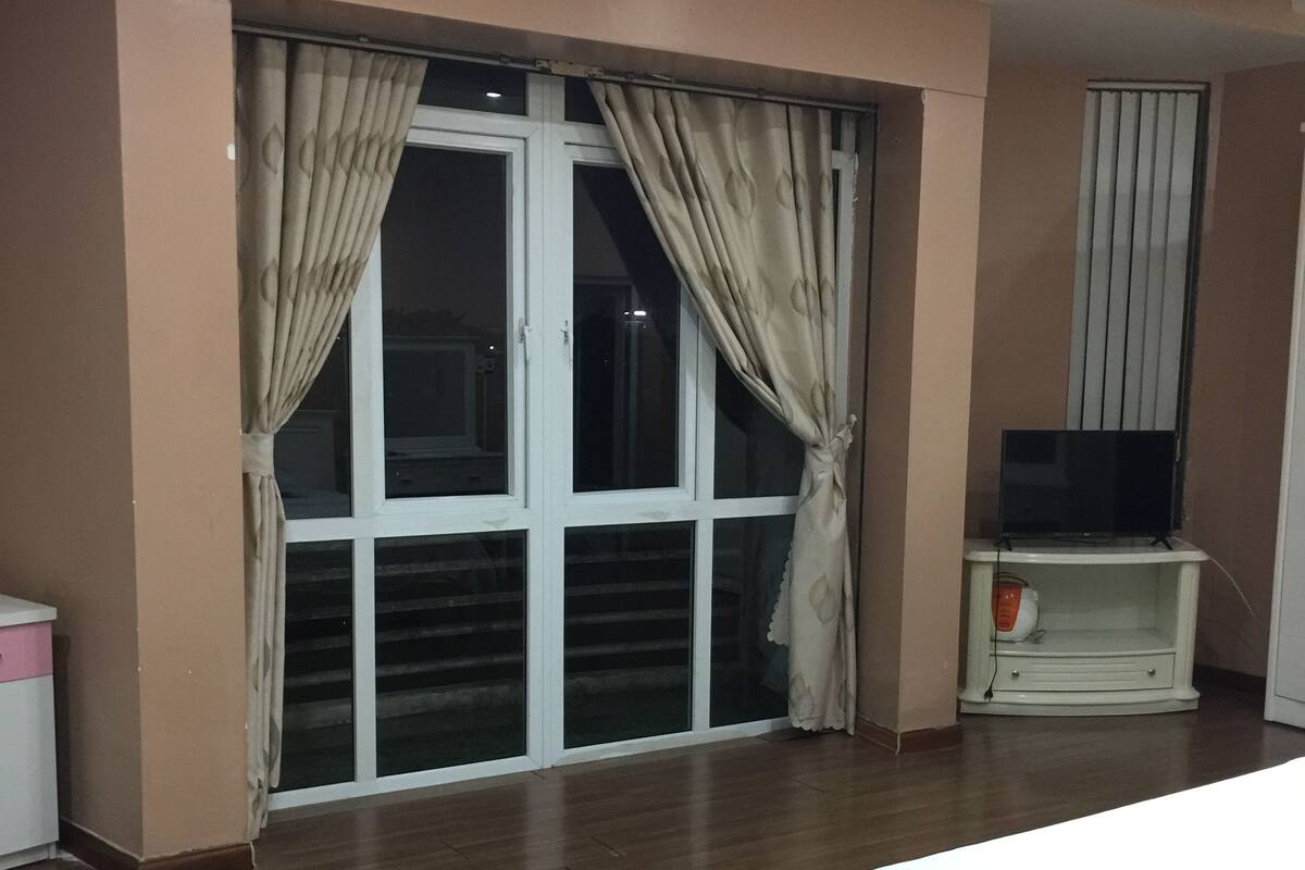 A bedroom with a bed, a TV on a stand, and a sliding glass door with curtains.